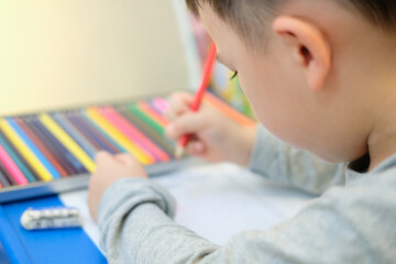 Naklejka premium A boy is drawing a picture with color pencil at home.