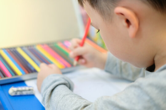 A boy is drawing a picture with color pencil at home.