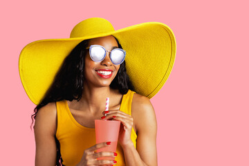 Portrait of a young smiling woman with yellow summer hat and sunglasses holding a drinking cup and...