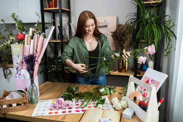 A girl florist with red hair collects a bouquet of roses in a flower shop. Remote workshop for the Assembly of bouquets.