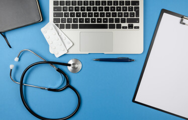 top view of desk of doctor or physician with stethoscope, laptop computer, book and clipboard with sheets of paper