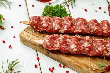 Raw lula kebab on skewers with spices on wooden board