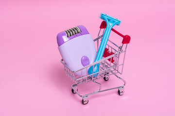 Purple epilator and blue razor in the supermarket trolley on a pink background. The concept of...