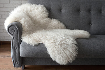 White sheep skin on a gray sofa. A cozy place to relax in the apartment. Modern Scandinavian style...