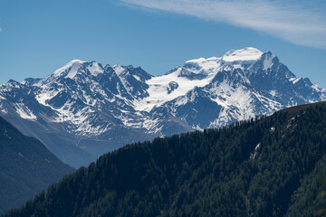 Alpine mountains, meadows and forests on a background of blue sky with clouds.