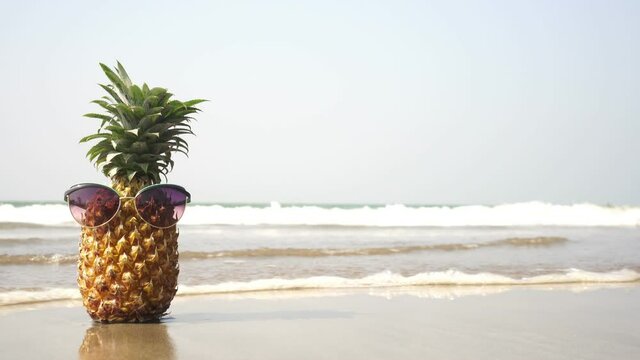 Fruit pineapple in glasses on a sandy beach against the background of the sea