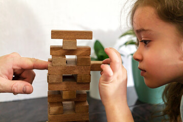 Father and daughter playing game Tumble tower from wooden block together