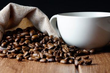white cup and coffee beans scattered on wooden surface. food and beverage concept