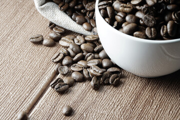 Coffee beans in a white cup and scattered on wooden surface
