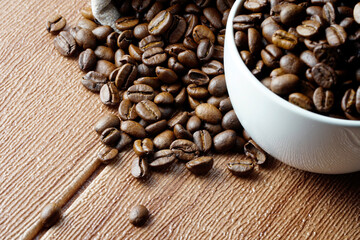 Coffee beans in a white cup and scattered on wooden surface