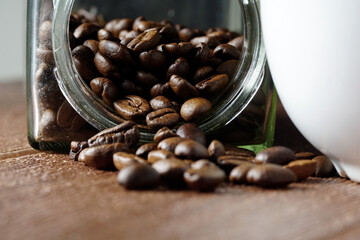 white cup and coffee beans scattered on wooden surface. food and beverage concept