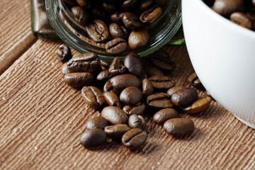 white cup and coffee beans scattered on wooden surface. food and beverage concept