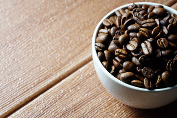 Coffee beans in a white cup on a wooden surface. Copyspace and international coffee day