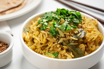 Kichari in a white plate on a light table near coriander and tortillas close-up