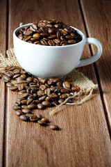 Coffee beans in a white cup on a wooden surface. Copyspace and international coffee day
