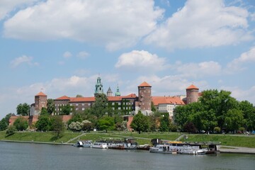 Fototapeta na wymiar Wawel Royal Castle in Krakow, Poland. Exterior view from the Vistula River. Barges with restaurants standing by the river bank.