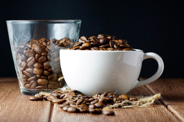 Coffee beans in a white cup and scattered on wooden surface