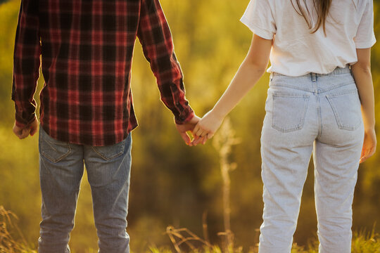 Cropped rear view image of a man and woman in casual clothing holding hands. Rear view of loving couple holding hands outdoors, on date in park. Shot from back of man and woman walking together.