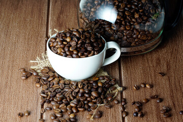 Coffee beans in a white cup and scattered on wooden surface
