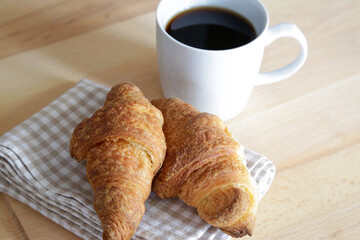 French croissant with a cup of black coffee, natural light on wooden table