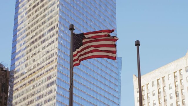 US flag waving in the shade attached to a pole. in the background the mirrored window facade of a New York skyscraper