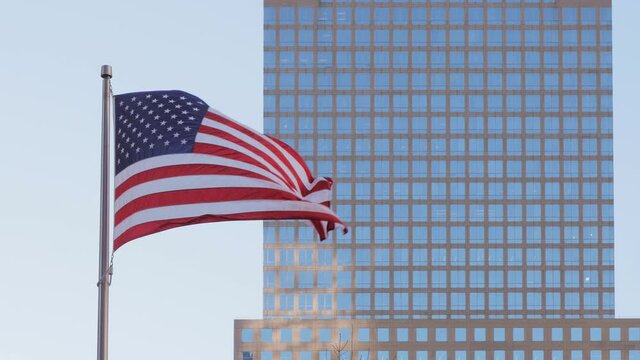 Frontal view of an American Stars and Stripes flag that waving in a sunny day with the mirror facade of a skyscraper and the blue sky as a background