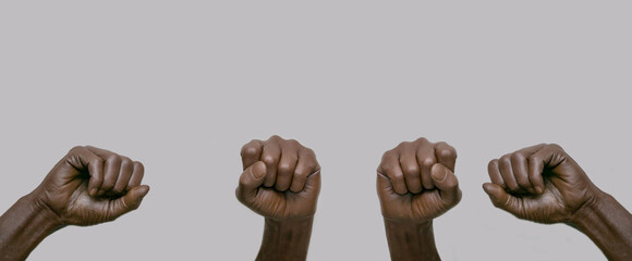 Black African-American human hands with raised fists in the air on a gray isolated background. Close-up, banner, copy space. The concept of protest, violence and struggle. - obrazy, fototapety, plakaty