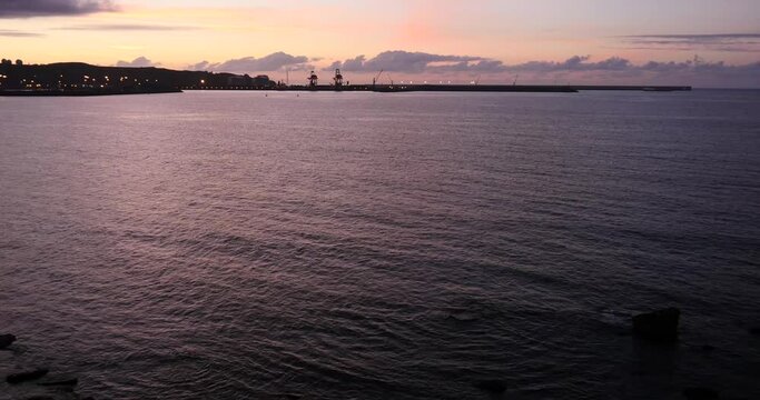 The evening light stains the Cantabrian sea, with the silhouette of the port of Gijon in the background (Asturias / Spain)