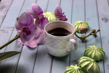 White coffee Cup. An Orchid on a wooden table. Orchid flowers and coffee. Still life with flowers, coffee and marshmallows. Black coffee. Marshmallows on a light wooden table. The view from the top.