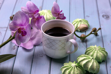 A Cup of coffee, marshmallows, and an Orchid on a light wooden table. top view.