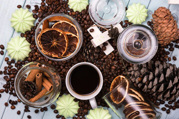 A white Cup of coffee on coffee beans, on a light blue wooden table. Wooden table. Fir cones on the table. Green marshmallows and white marshmallows. Dried citrus. Brown background.