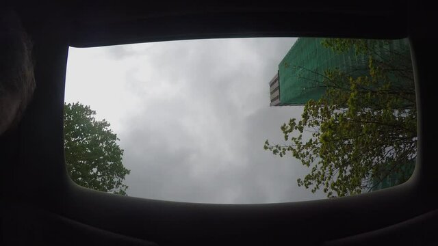 View of the grey cloudy sky through opened sunroof of the moving car.