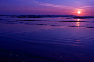 Fototapeta premium Seascape nature during a sunset on an empty ocean beach with gentle waves lapping at the shore. Very peaceful, as sun is above to dip below the horizon.