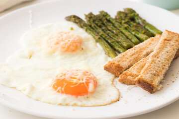 Fried eggs, fresh crunchy asparagus and toast bread on a white plate