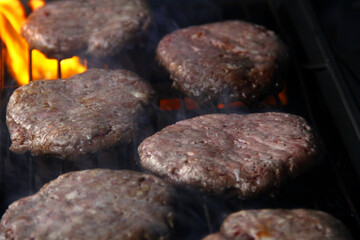 Fresh hamburger patties being grilled over fire
