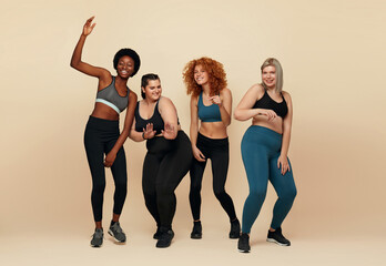 Fototapeta premium Diverse. Different Women Dancing Portrait. Diversity Figure And Size Models Full-Length Portrait. Group Of Multicultural Friends In Sportswear Posing On Beige Background. Body Positive As Lifestyle.