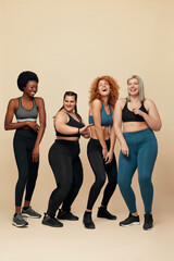 Fototapeta na wymiar Body Positive. Diversity Women With Different Figure And Size Full-Length Portrait. Group Of Multi-Ethnic Girls In Sportswear Against Beige Background. Dancing And Sport As Lifestyle.