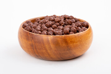 Wooden bowl with chocolate corn balls and spoon on white background