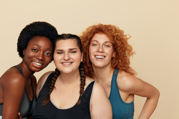 Fototapeta na wymiar Women. Group Of Diversity Models Portrait. Smiling Multiethnic Female In Fitness Clothes Posing On Beige Background. Body Positive As Lifestyle. 