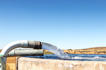 A Large stream of water gushing out of a pipe and filling a cement farm dam closeup
