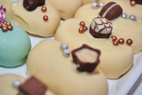 Luxurious small white chocolate glazed mini cakes. Fancy decoration. Modern and contemporary style. Delicious sweets for gourmet event catering.