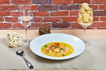 Soup with seafood sun-dried tomatoes and shrimp on a white plate. with a glass of water