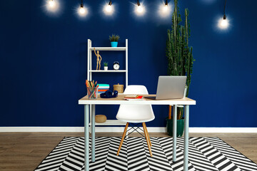 Working table with laptop against blue wall in modern flat