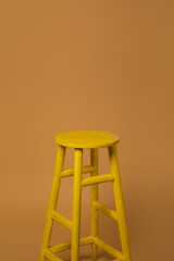 Photo of a yellow bar photography stool isolated on a beige background.