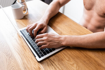 Fototapeta na wymiar cropped view of shirtless freelancer working on laptop on kitchen with coffee