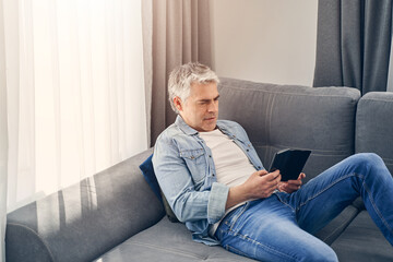 Grey haired man sitting on sofa and relaxing