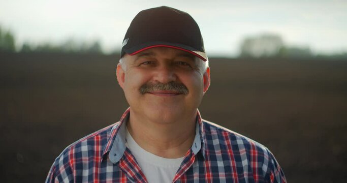 A male farmer in a baseball cap and looking at the camera smiling after a working day.