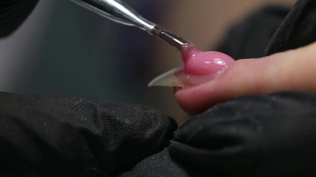 Professional manicure. Nail extension. Close-up of applying a drop of pink nail Polish with a brush to one nail. Procedure for making long artificial gel nails in a modern beauty salon.