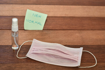Pink face mask with sanitizer on wooden background. New normal concept image. 