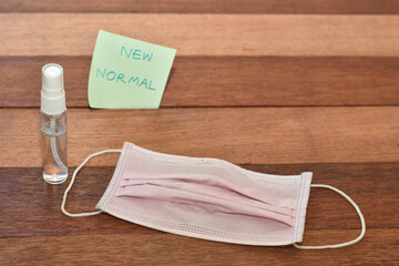 Pink face mask with sanitizer on wooden background. New normal concept image. 